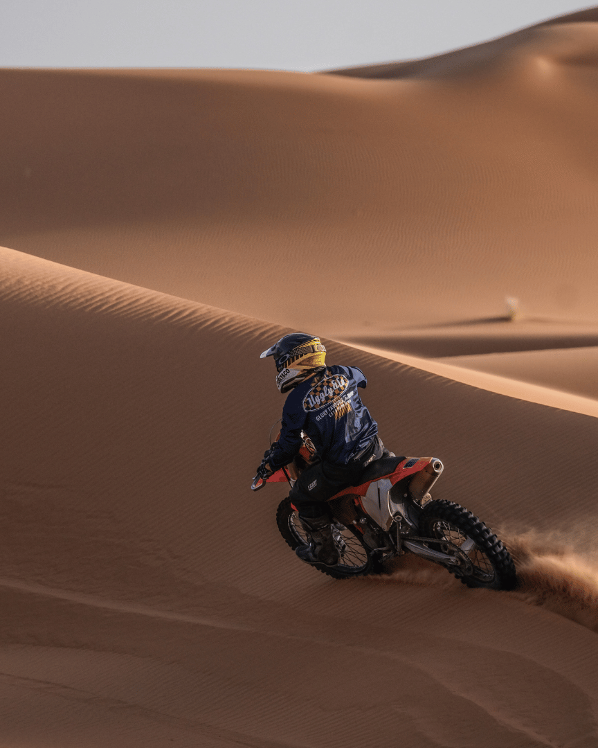 MX rider in the desert in a blue motocross jersey and the brand name 'Uggly&Co Motorcycle Clothing' on the front