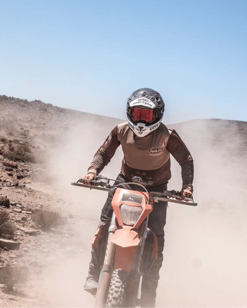 Front view of a person standing up while riding a motocross bike in the desert in an Uggly&Co MX shirt