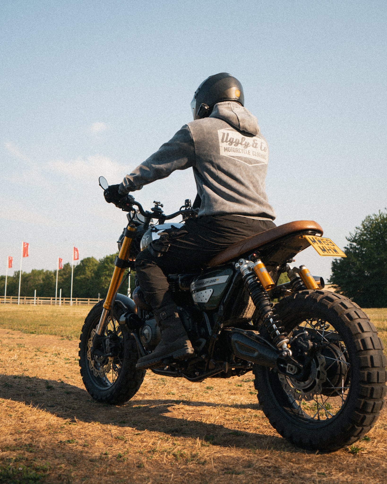 Man wearing an acid wash hoodie sitting on a Triumph Scrambler motorcycle at sunset.