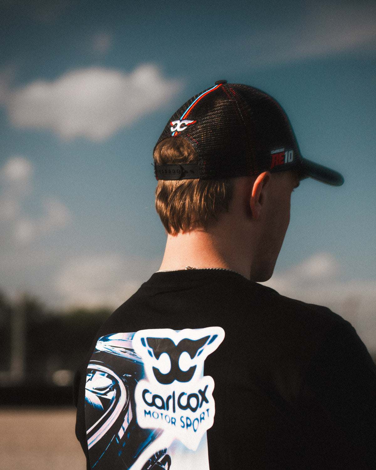 Side profile of the Carl Cox x Alpha Racing & Simon Reid Trucker Hat, showcasing its structured shape, curved peak and classic motorsport headwear design.
