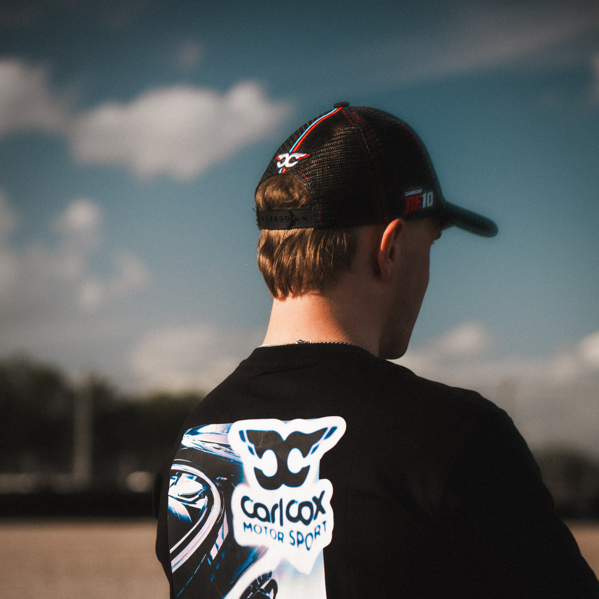 Side profile of the Carl Cox x Alpha Racing & Simon Reid Trucker Hat, showcasing its structured shape, curved peak and classic motorsport headwear design.