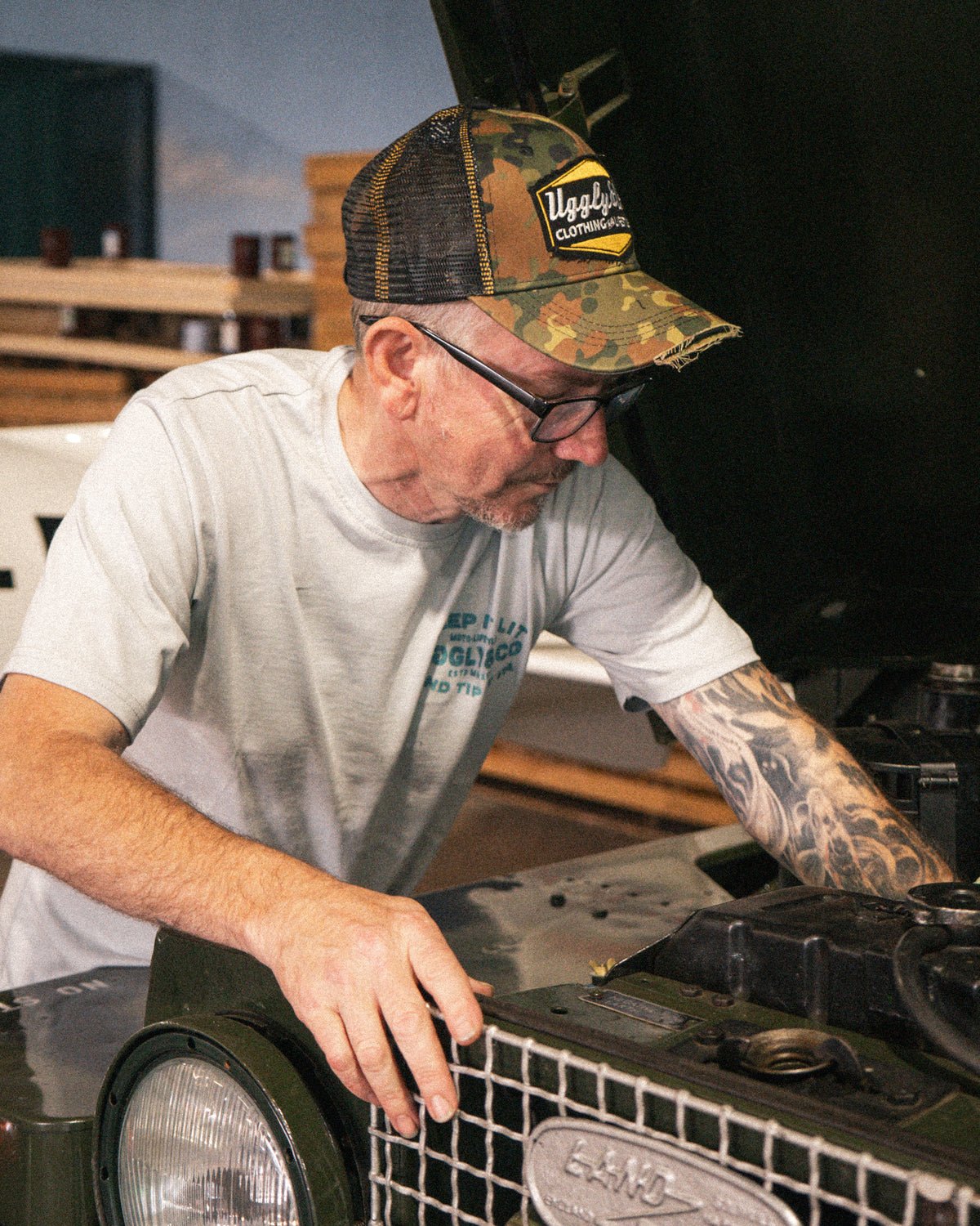 Uggly & Co Green Camo Diamond Trucker Hat worn by a man working on a Land Rover.