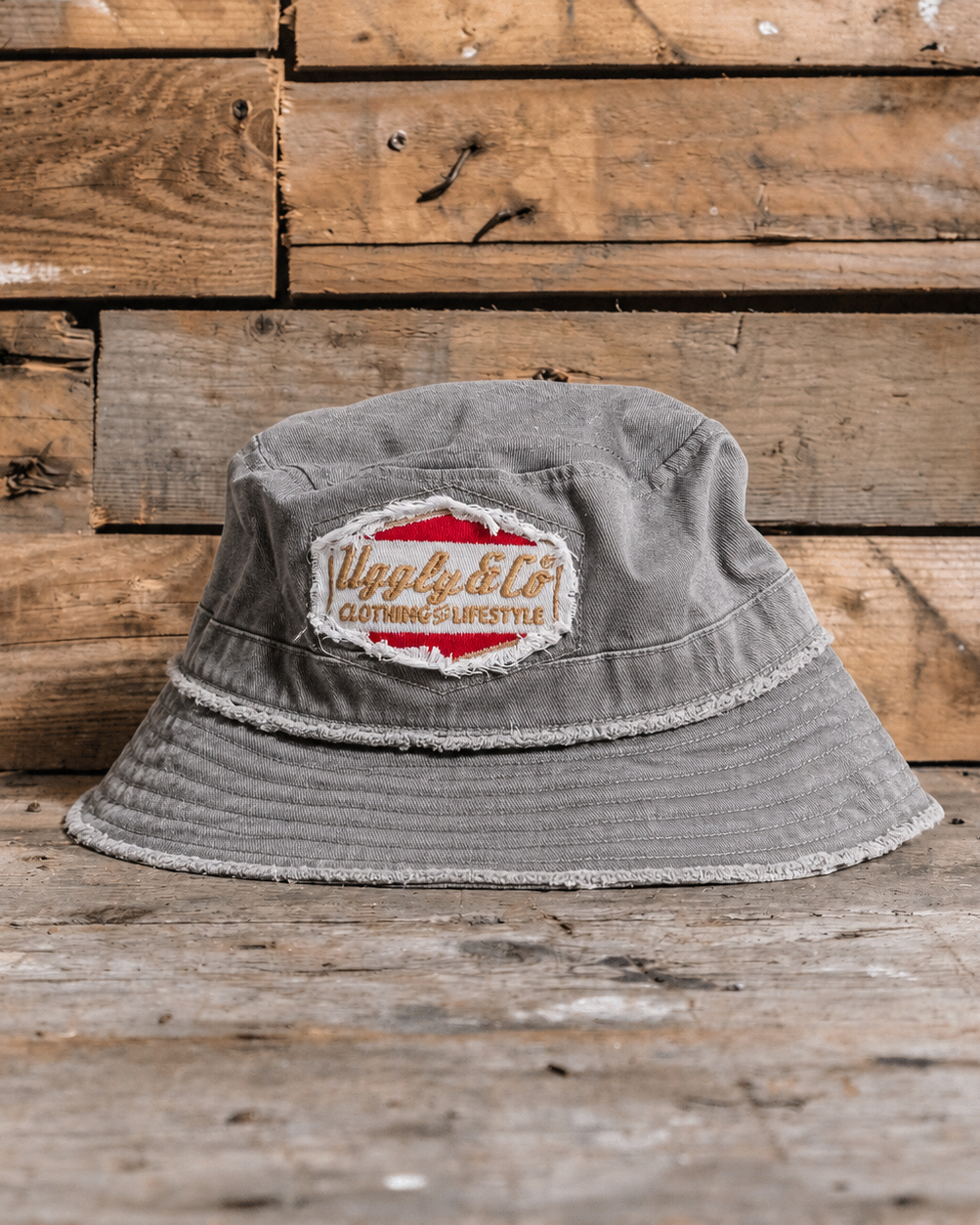 Distressed grey bucket hat with an Uggly&Co diamond logo on a wooden background