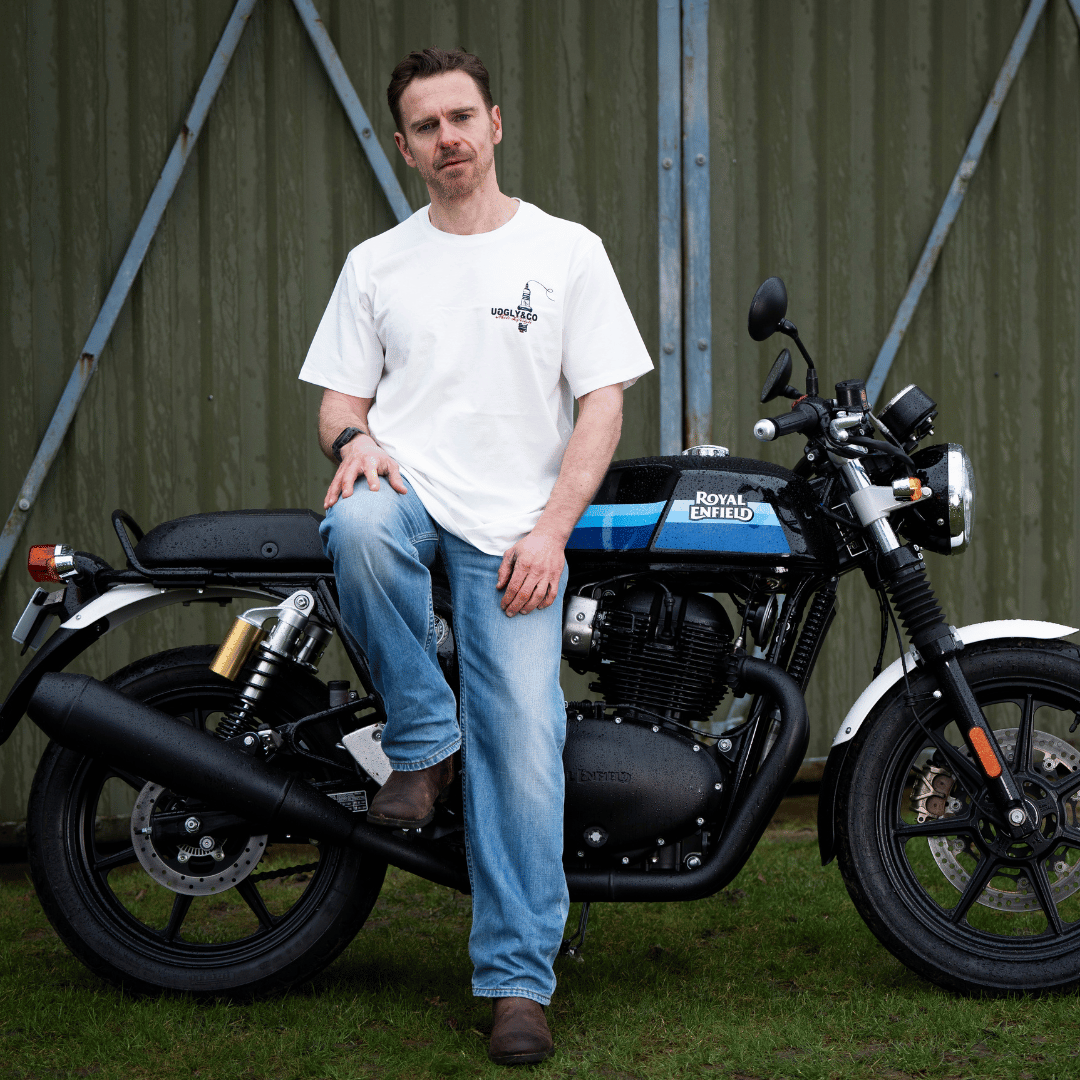 Rear view of a model wearing a limited edition Valentine’s white t-shirt with spark plug heart graphic, and Uggly&Co logo while sitting on a motorcycle