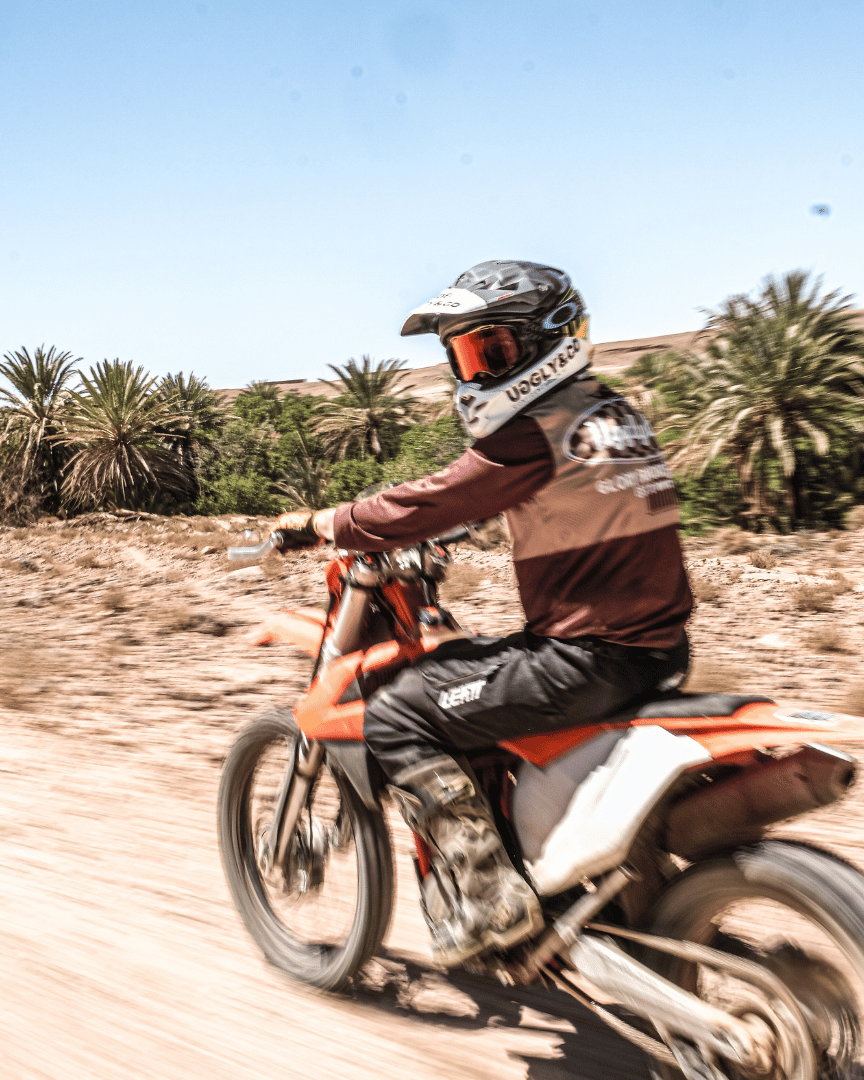 A person riding a motocross bike in a long-sleeved brown and beige motocross jersey in the desert