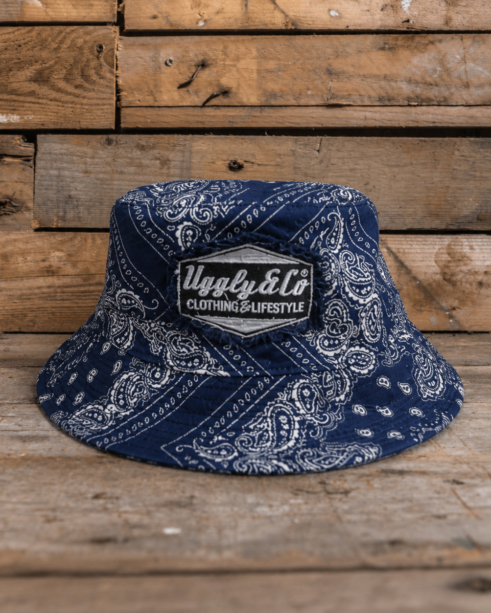 Blue bandana-patterned bucket hat with a brand logo on a wooden background