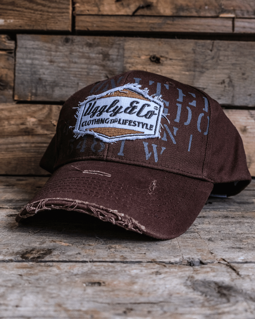A brown 'Aviation' Diamond Trucker Hat with the Uggly&Co logo on the front, placed on a wooden surface.