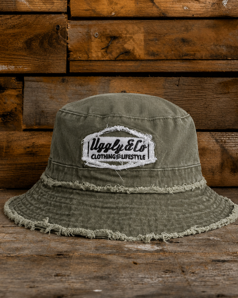 Frayed green bucket hat with an Uggly&Co diamond logo on a wooden background