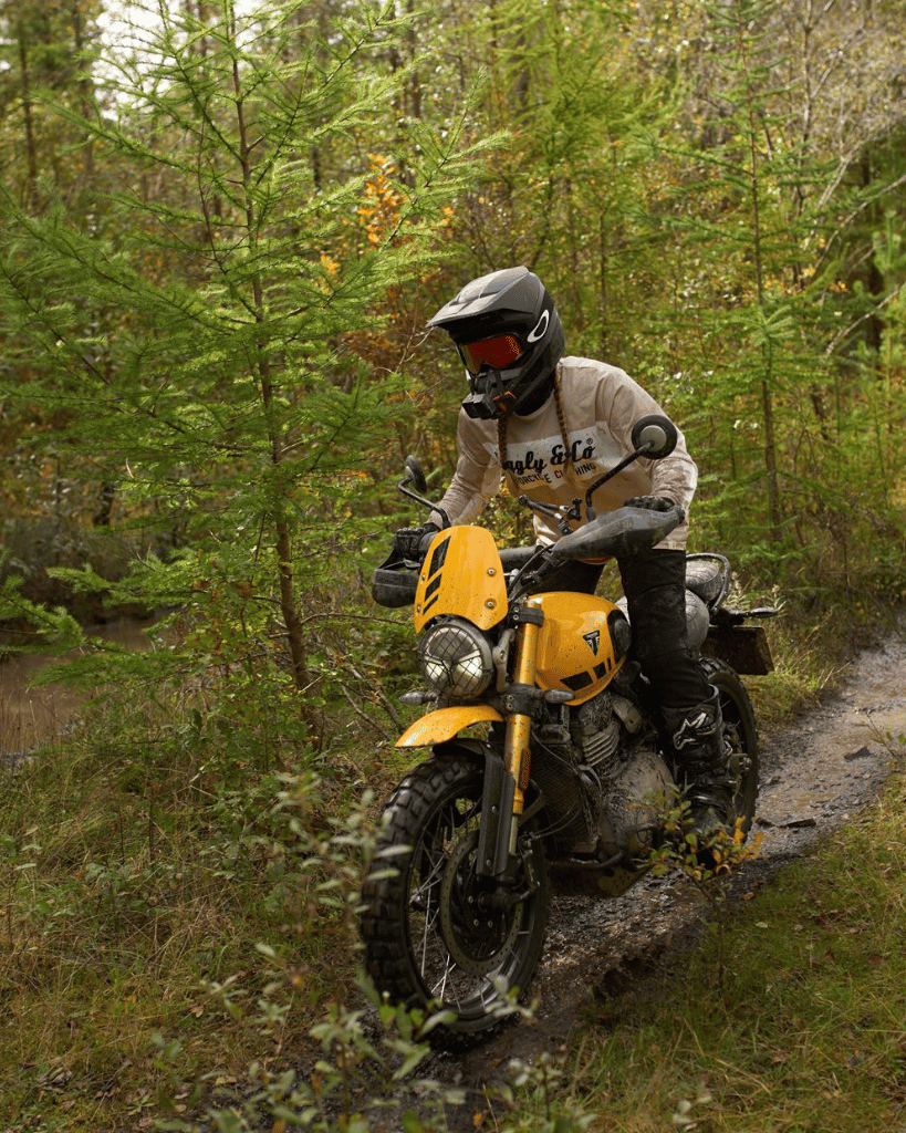 Person riding a yellow motorcycle on a forest trail in an MX shirt