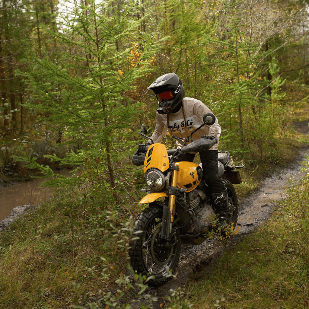 Person riding a yellow motorcycle on a forest trail in an MX shirt