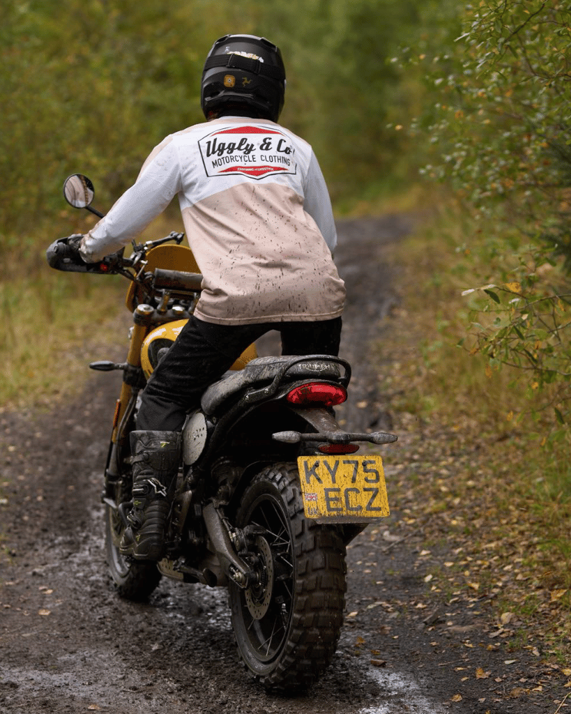 Person riding a motorcycle on a dirt road with a helmet and jacket and MX shirt