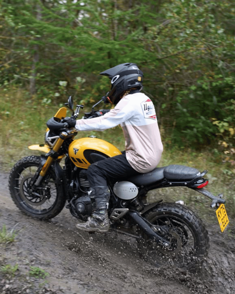 Person riding a yellow motorcycle on a muddy trail with greenery in the background