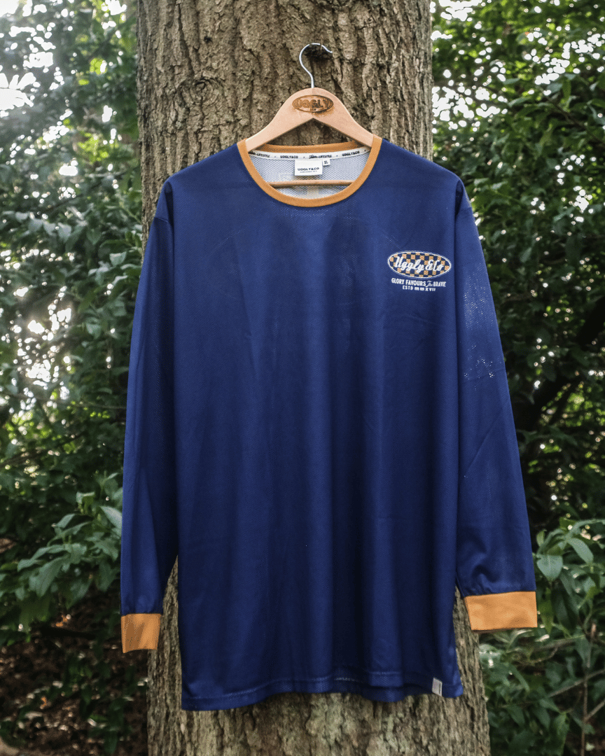 A blue and yellow long-sleeved motocross jersey hanging on a tree forwards with graphical designs and text on the back.