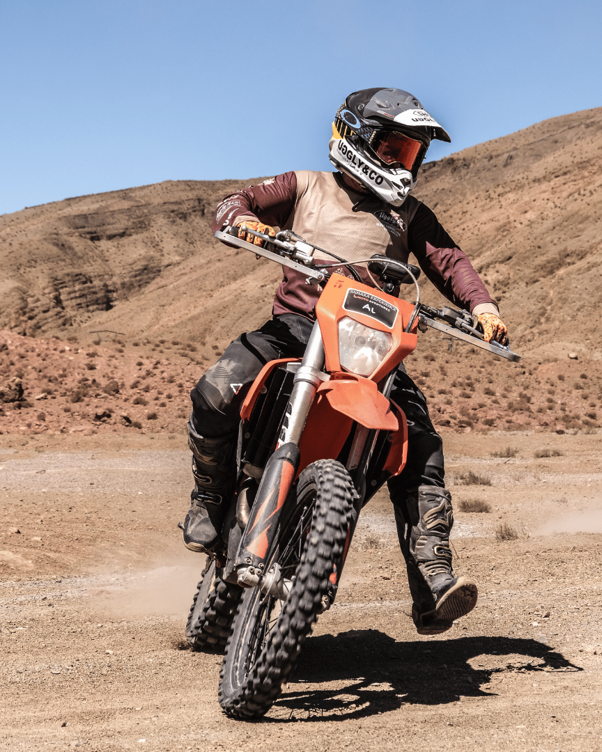 A person riding a motocross bike in the desert in a brown Uggly&Co MX shirt, front view
