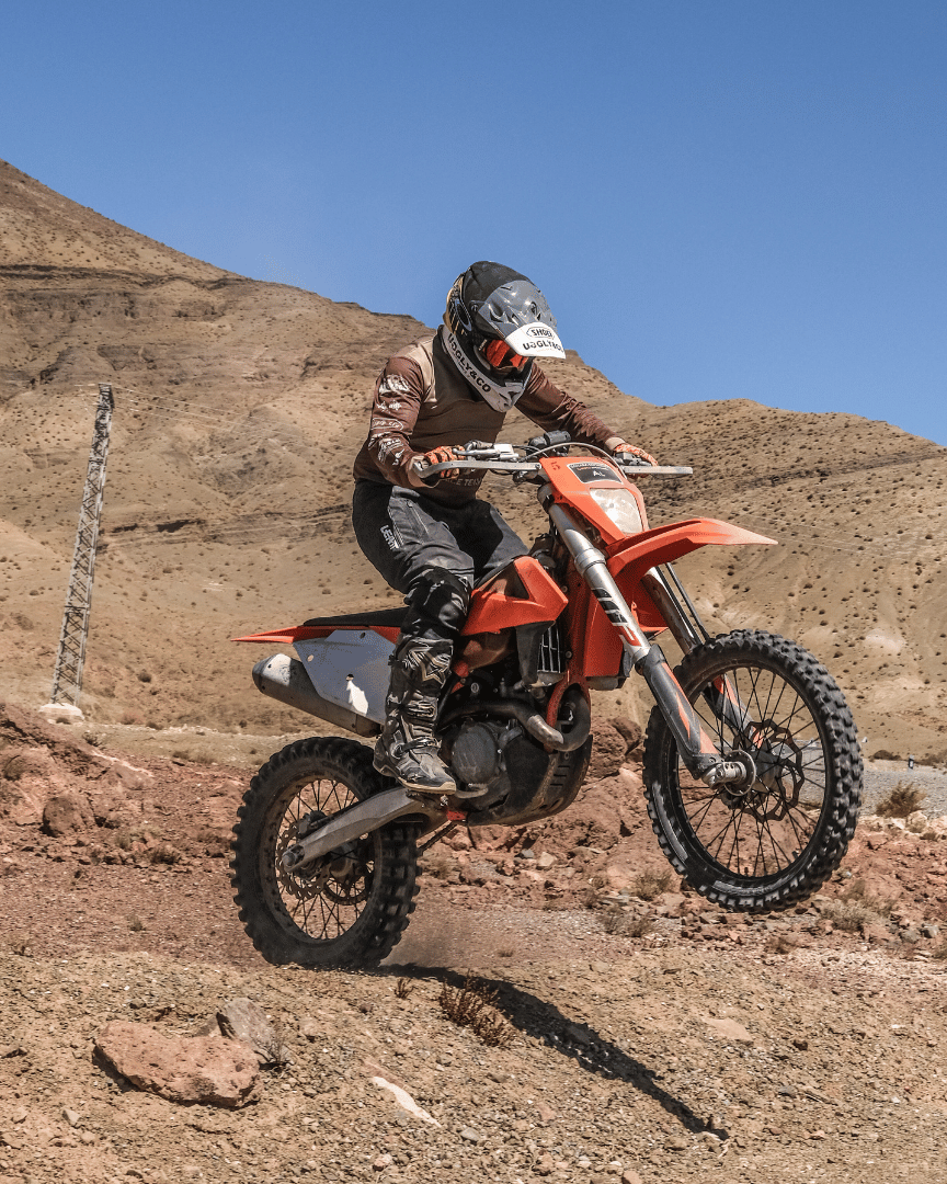 A person jumping a motocross bike in the desert in a brown MX shirt