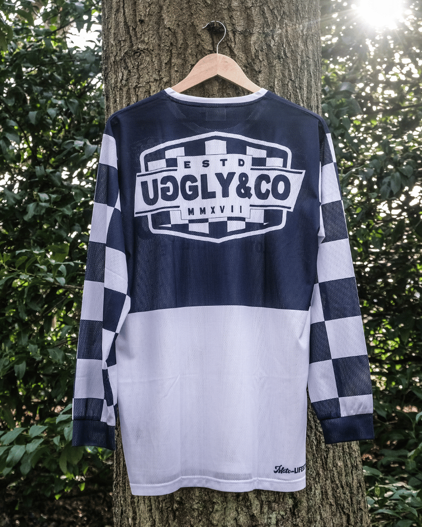 Backwards facing checkered long-sleeve MX shirt with an Uggly&Co brand logo hanging on a tree