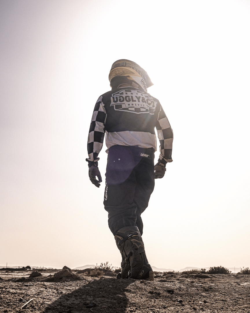 Motocross rider in full gear in the desert wearing a chequered Uggly&Co MX shirt facing backwards