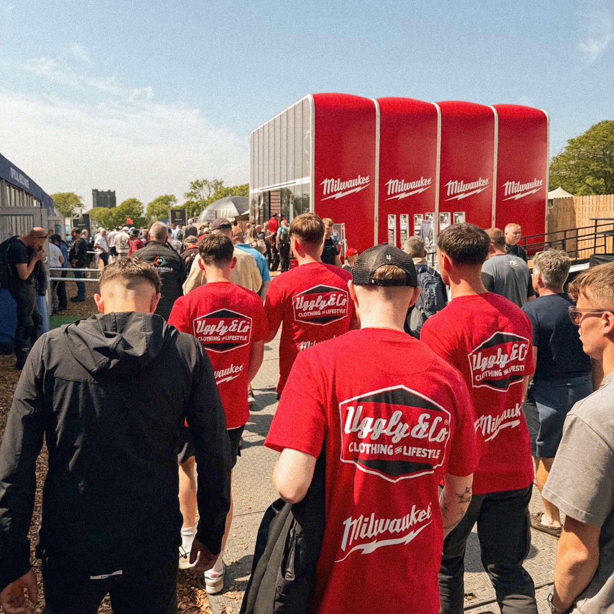 race fans wearing red Milwaukee collaboration t-shirts walking through a busy motorcycle event paddock on a sunny day
