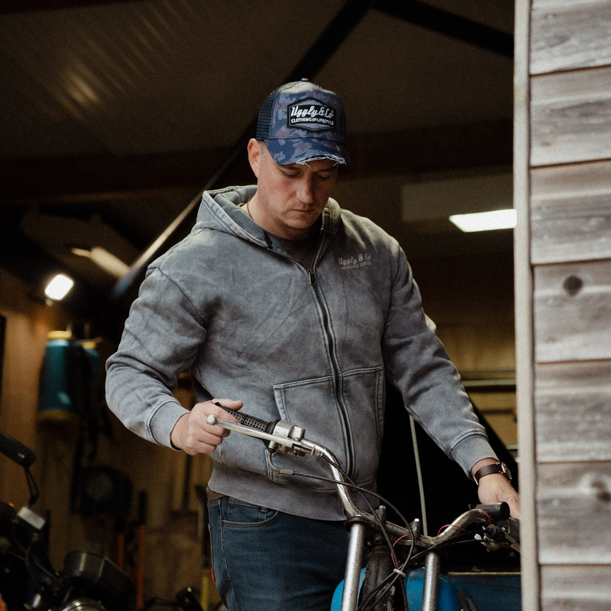 Blue camo trucker hat worn by mechanic working on a vintage motorbike