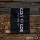 A rectangular black flag with the 'Carl Cox Motorsport' logo in white and red, displayed on a wooden surface.