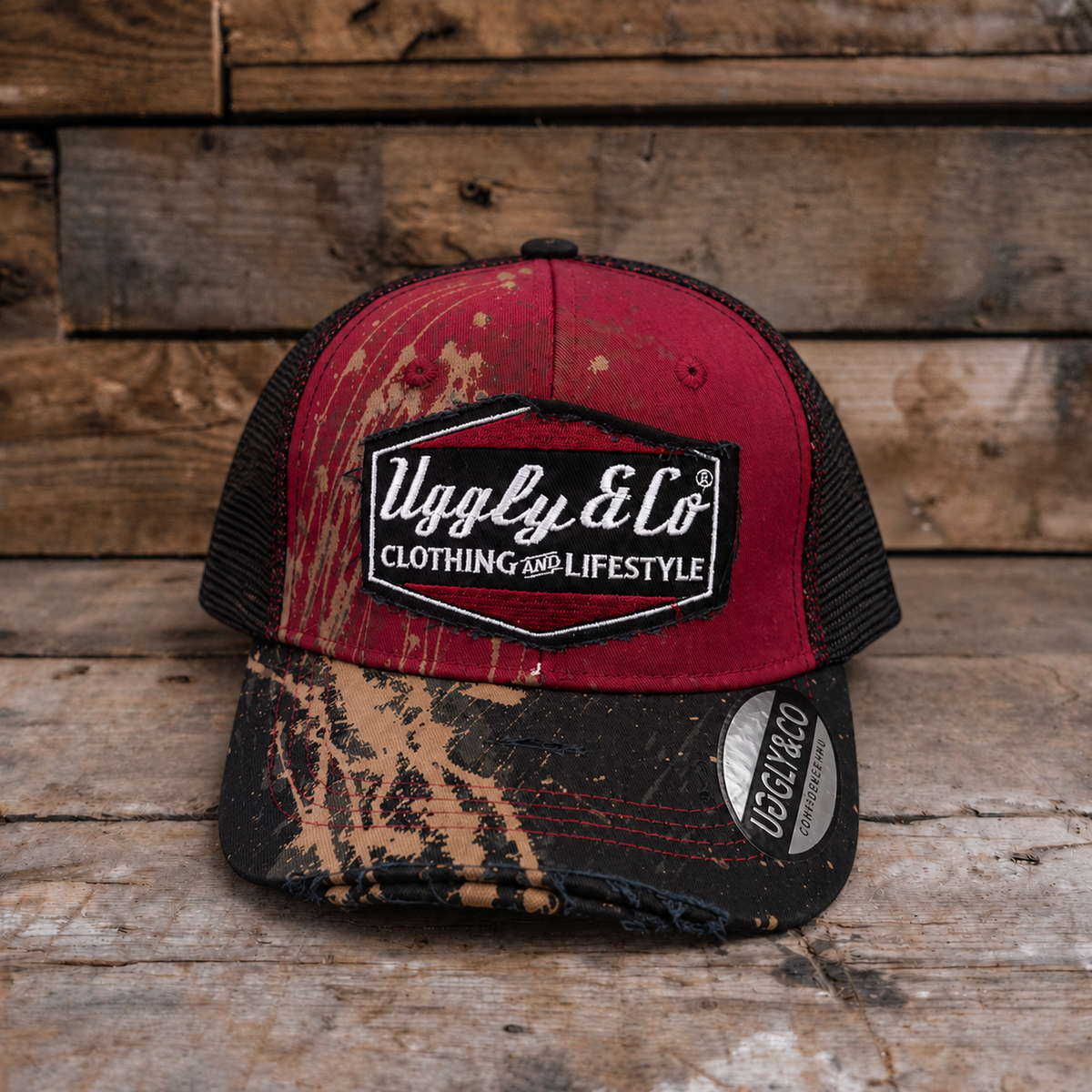A trucker-style cap with a distressed red front panel, black mesh back, and a camouflage-patterned brim, displayed on a rustic wooden surface.