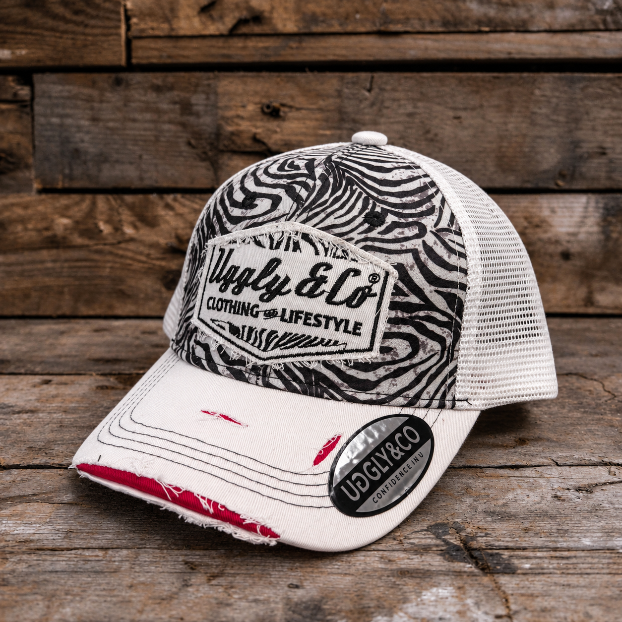 A trucker-style cap with a black and white zebra-patterned front panel, white mesh back, and a white brim with distressed edges and red stitching. The front patch reads 'Ugly & Co Clothing and Lifestyle.