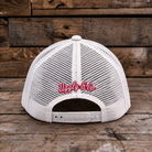 White mesh trucker hat shown from the back, featuring red embroidered cursive text reading 'Ugly & Co.' on the center back, photographed against a rustic wooden plank background.