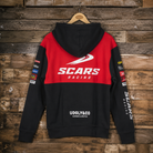 A black and red hooded sweatshirt shown from the back, hanging on a wooden hanger against a rustic wood plank wall. The hoodie features a bold red upper back with a large white 'SCARS RACING' logo, black sleeves, and multiple sponsor-style patches on the sleeves.