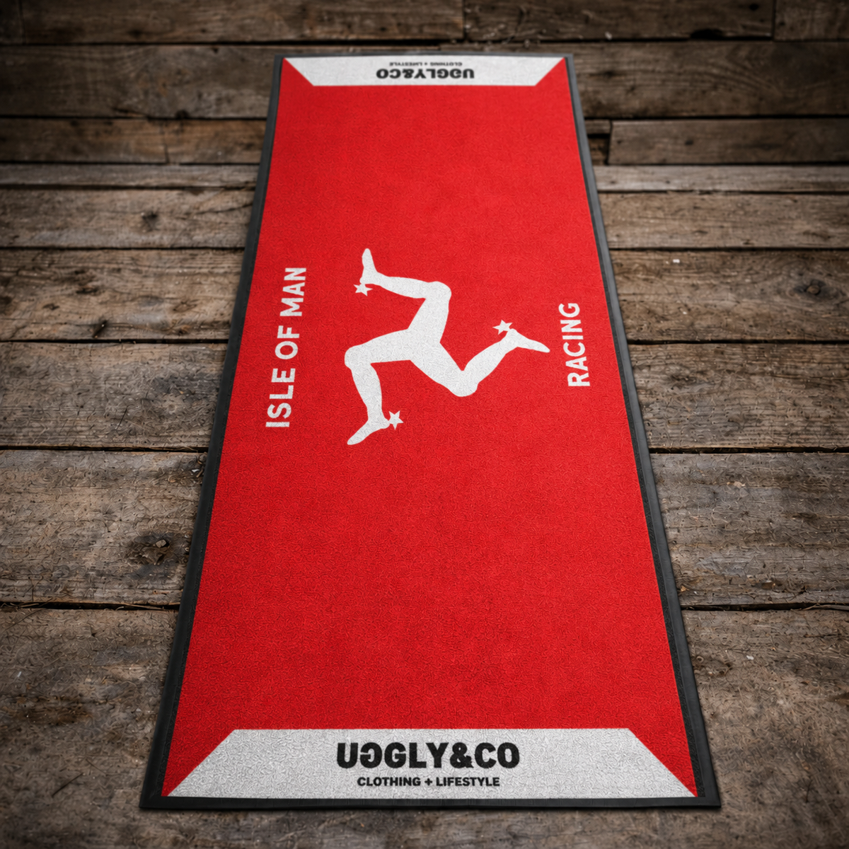 Red mat with white graphic and text on a wooden surface, featuring 'Uggly & Co' branding & Isle of Man Racing, with the Manx Isle of Man Logo.