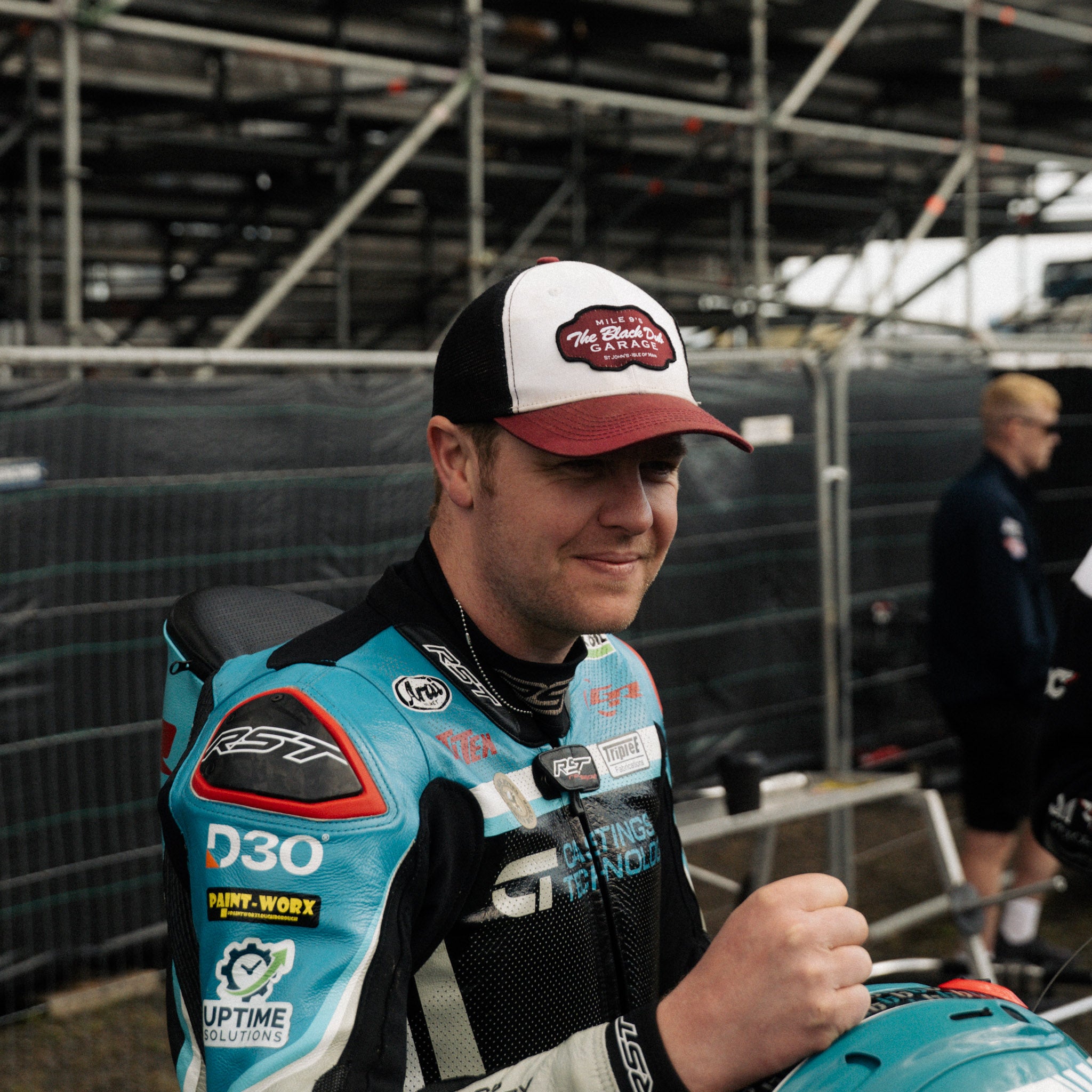 Dan Ingham in black dub hat by pit lane and race stands from side profile 