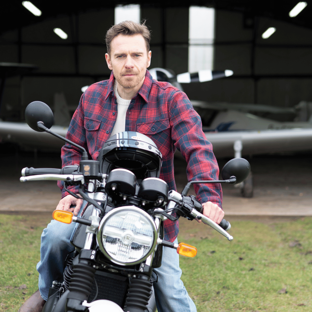 Man in a red plaid shirt sitting on a motorcycle with airplanes in the background