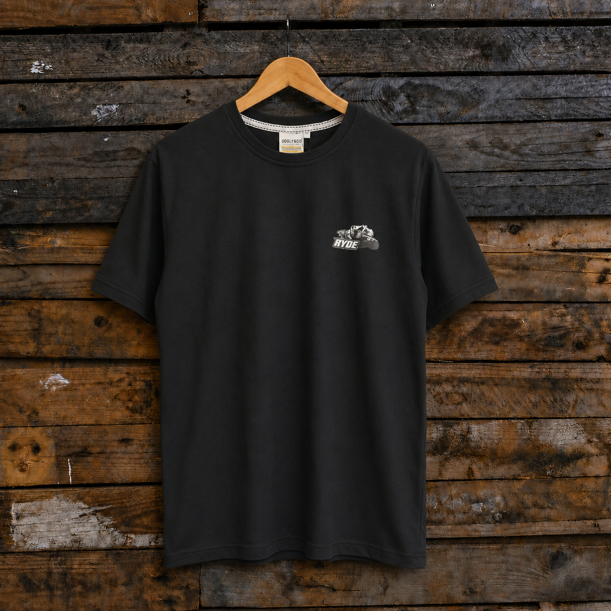 Front view of an Uggly&Co black t-shirt with Kyle Ryde graphic design on a wooden background