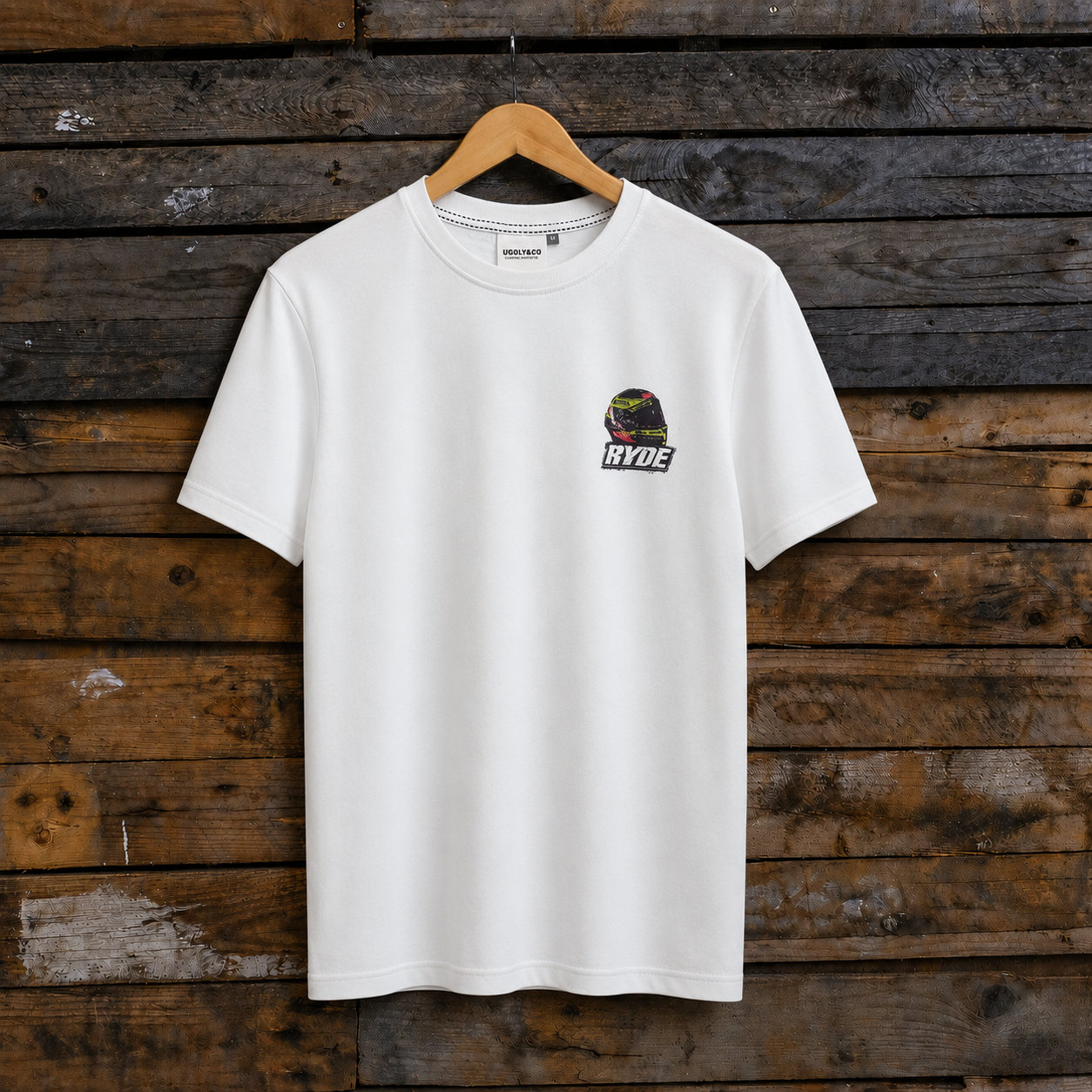 Front view of a Kyle Ryde signature white t-shirt with motorbike helmet graphic and Ryde logo on a wooden background