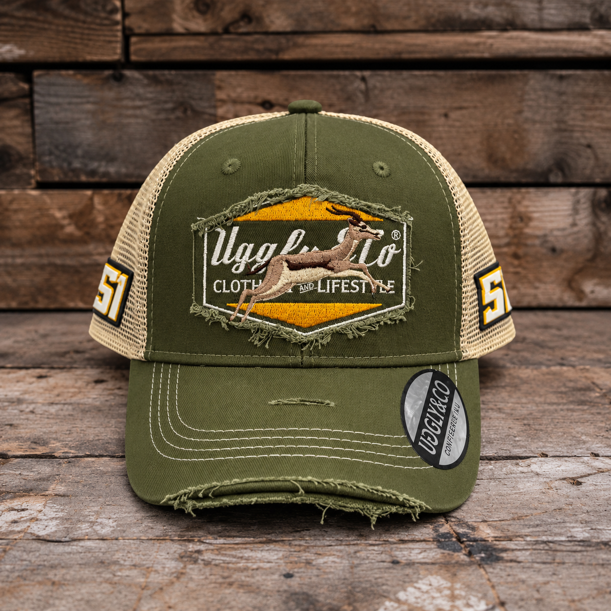 An olive green and beige trucker-style baseball cap with a distressed, frayed look, featuring a large embroidered patch on the front with a deer graphic and the text 'Uggly & Co'. The side panels have '51' printed on them, and a 'Clothing & Lifestyle' sticker is visible on the brim, set against a rustic wooden background.