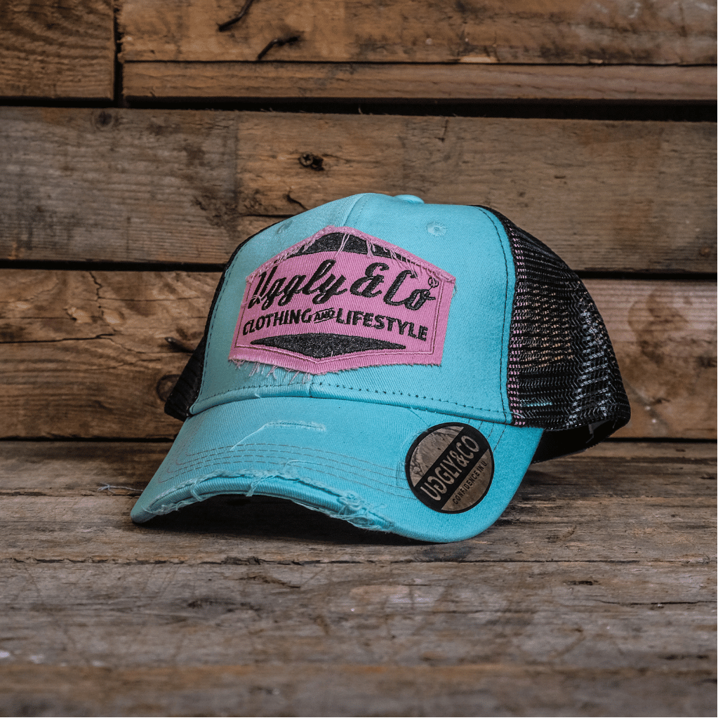 Turquoise trucker hat with pink logo on a wooden surface