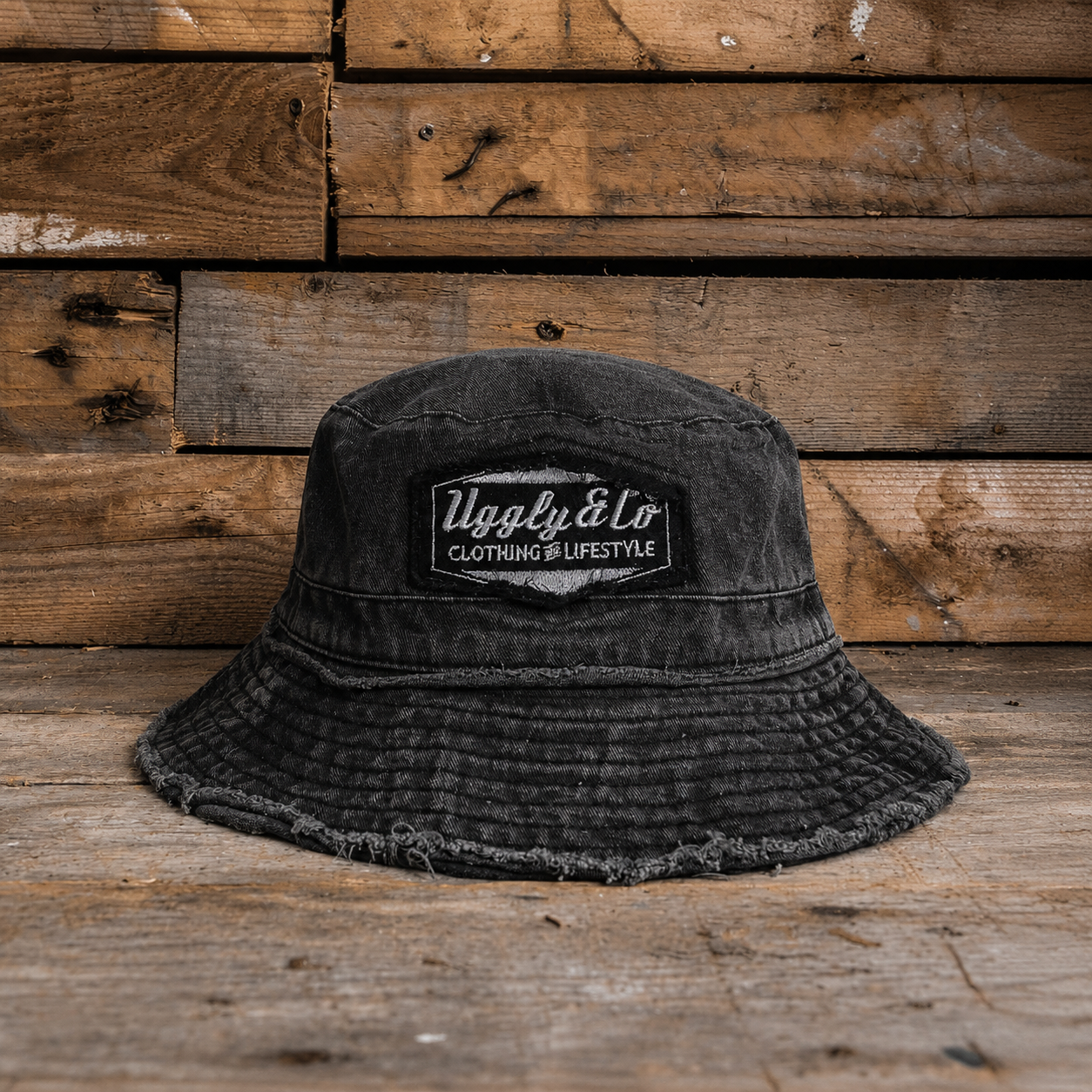 Acid washed distressed black bucket hat with an Uggly&Co logo on a wooden background