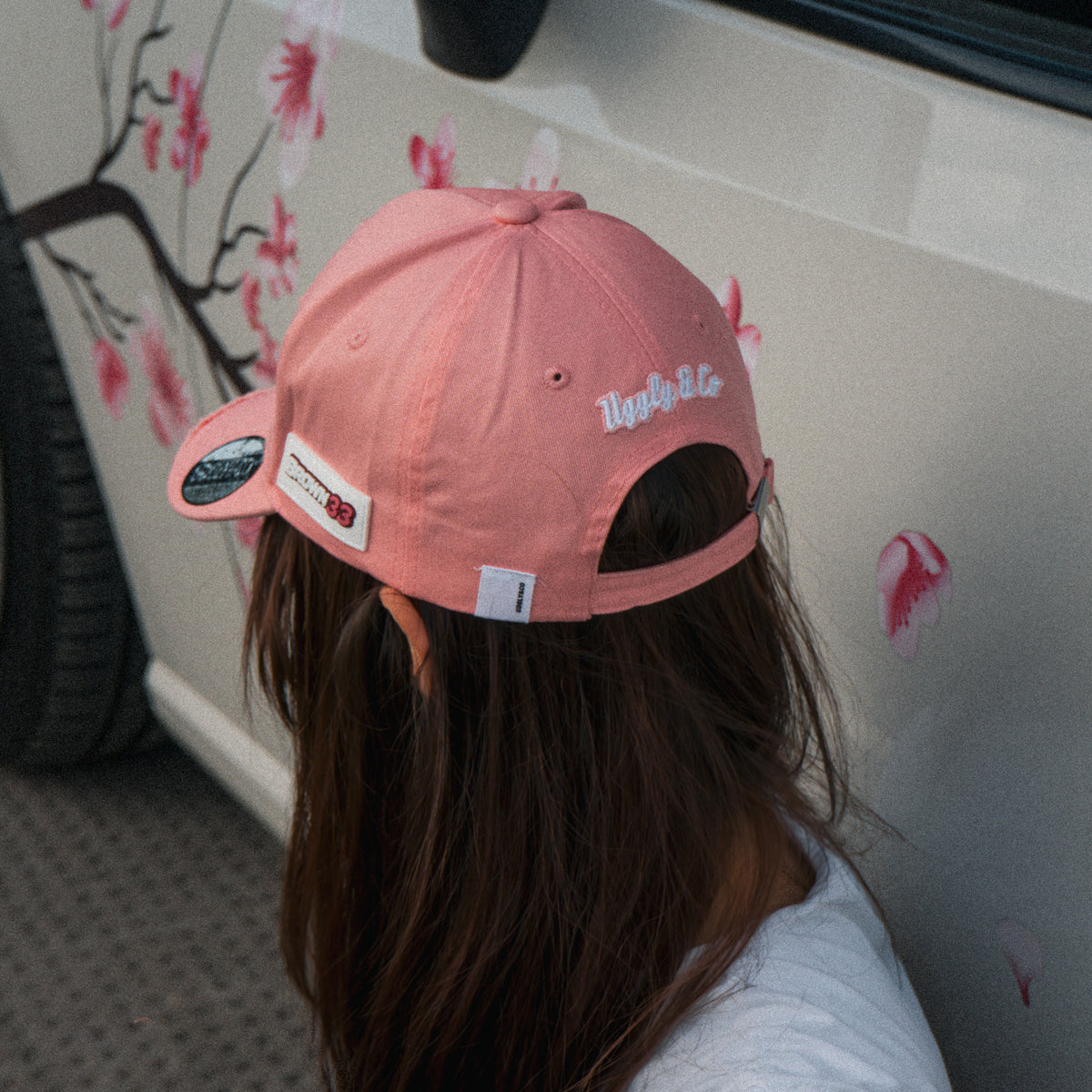 Women’s lifestyle photo featuring the Washed Pink Vintage Cap in front of a modified car