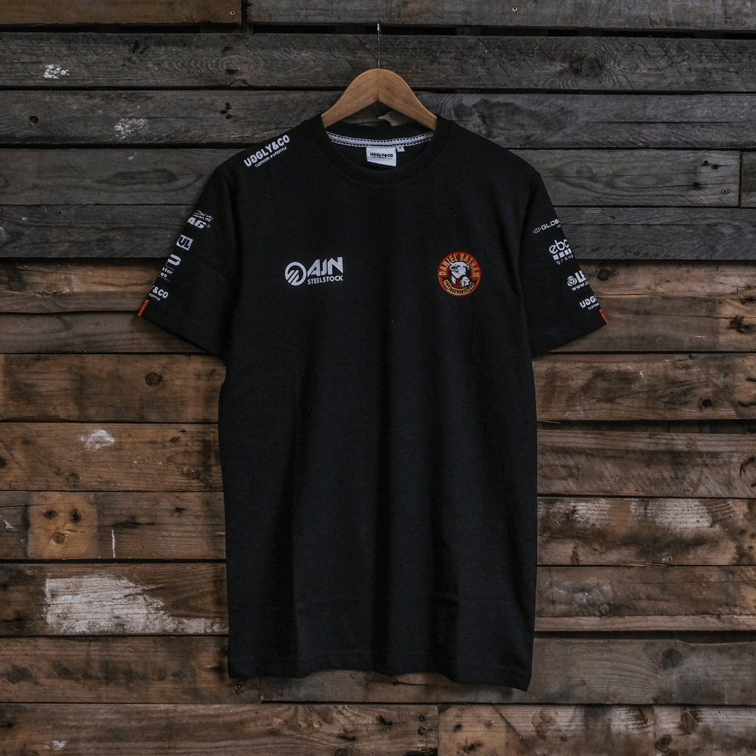 Front view of a Banthams Racing branded black t-shirt with racing sponsor logos on a wooden background