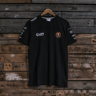 Front view of a Banthams Racing branded black t-shirt with racing sponsor logos on a wooden background