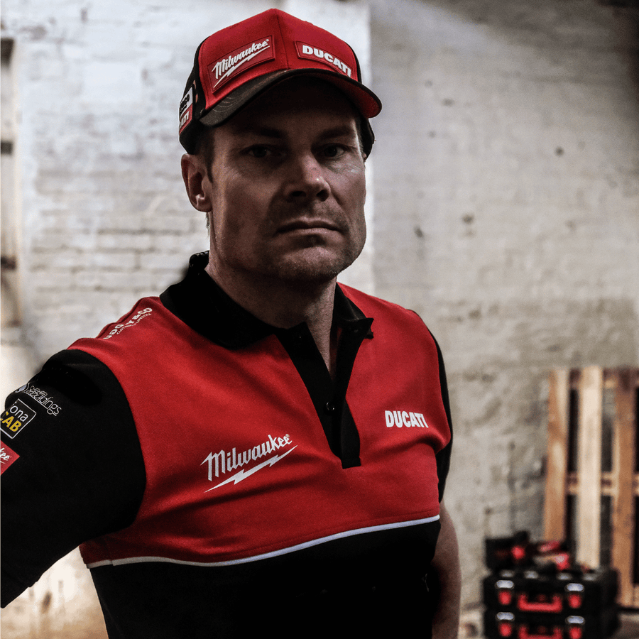 A model looking straight at the camera while wearing a Milwaukee x Ducati polo shirt, featuring a black lower half and a red upper torso in a warehouse