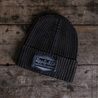 Black beanie with a brand patch on a wooden surface