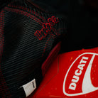 Product photo of the Black & Red Flat Track Trucker Hat on a rustic wooden background, showing its black and red racing style.