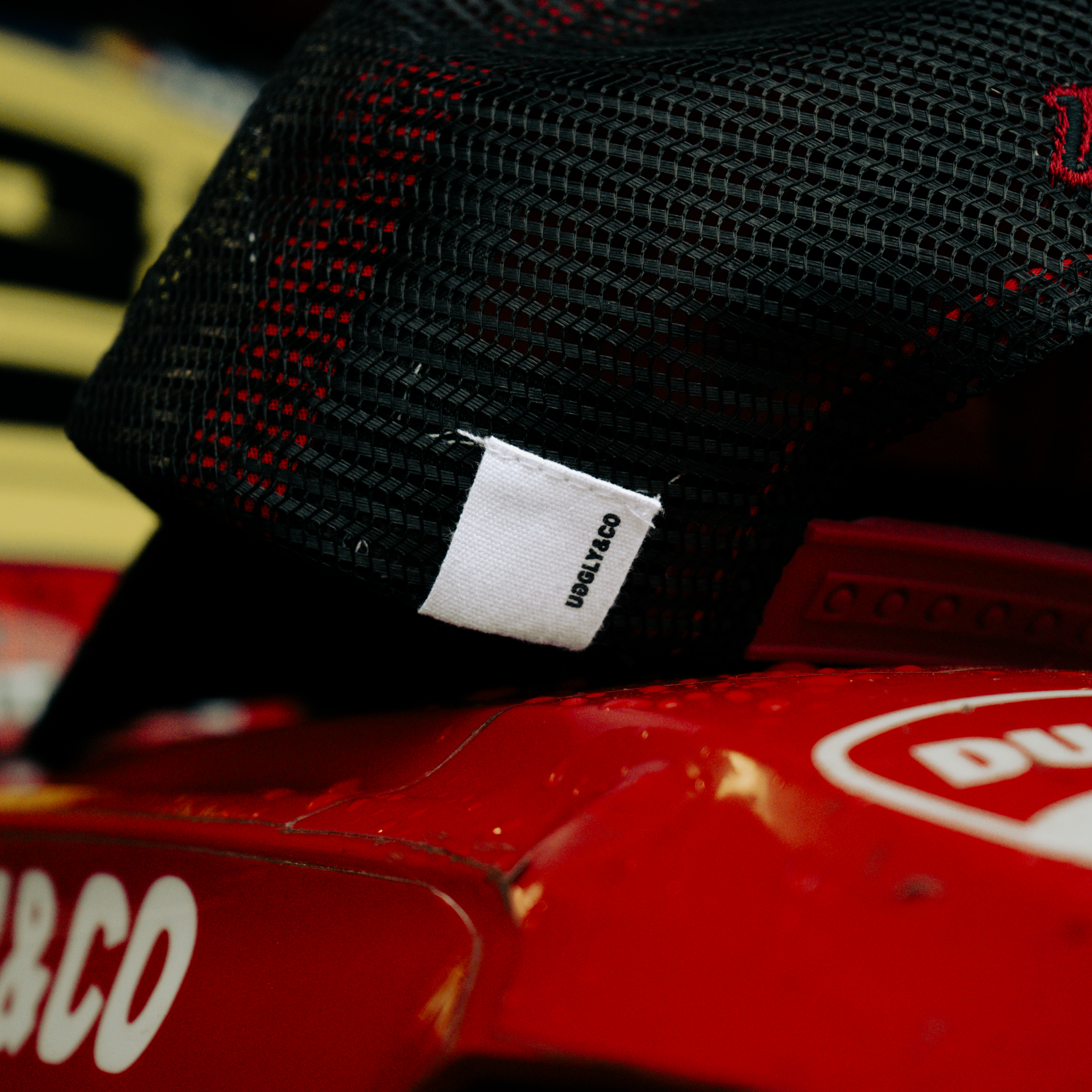 Uggly&Co Black & Red Flat Track Trucker Hat with mesh back, curved peak, red detailing and a bold flat track-inspired design.