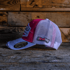 Side view of a Bradley Ray branded pink and white cap with Uggly&Co diamond logo on the front on a wooden background