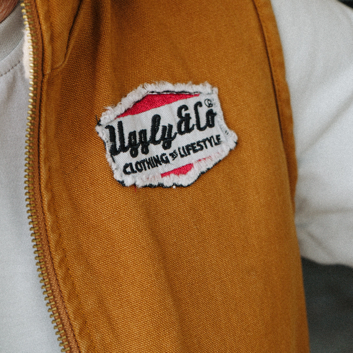 Close up of the Uggly & Co logo detail on the Brown Workwear Canvas Gilet, highlighting the branding and durable canvas material of this motorcycle lifestyle workwear piece.