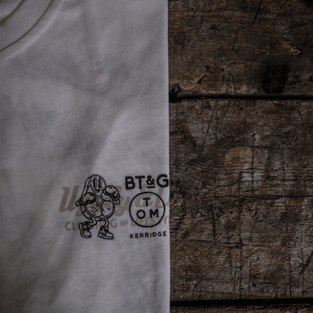 Close up of the chest logo on a Tom Kerridge's Butchers Tap and Grill white t-shirt with black graphics and text on a wooden background