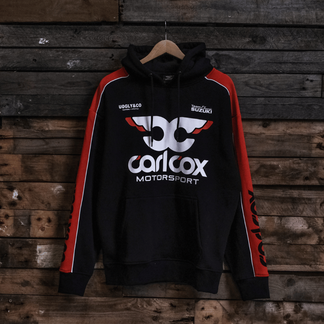 Black hoodie with red sleeves featuring Carl Cox Motorsport branding on a wooden background