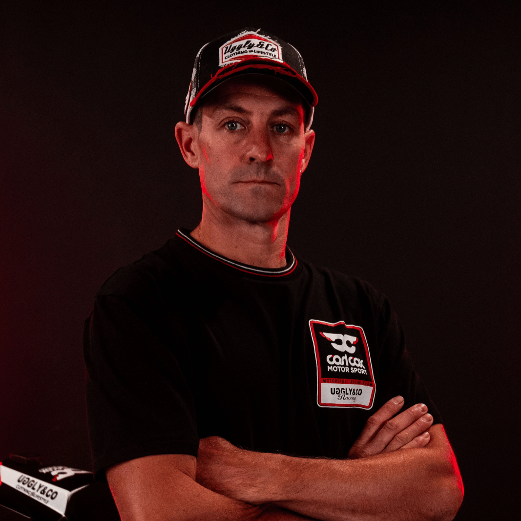 A model wearing a Carl Cox motorsport black t-shirt with an Uggly&Co logo looking at the camera
