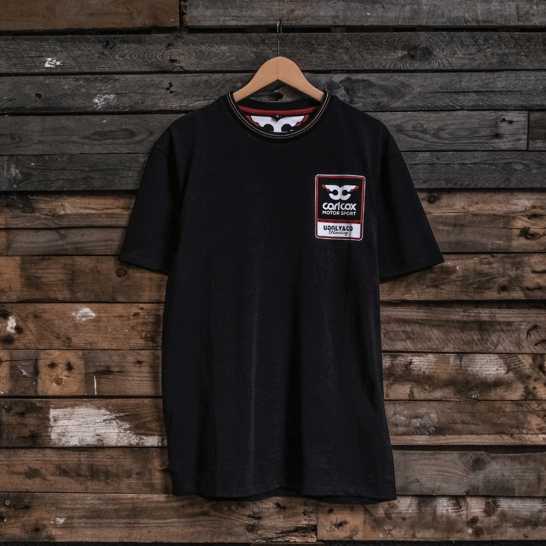 Front view of a Carl Cox motorsport black t-shirt with an Uggly&Co logo on a wooden background