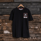 Front view of a Carl Cox motorsport black t-shirt with an Uggly&Co logo on a wooden background
